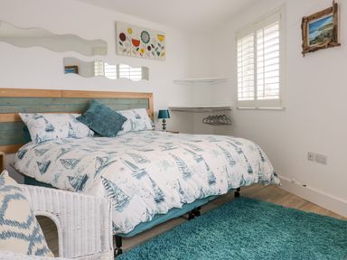 A bedroom with a bed covered in sailboat patterned bedding a white wicker chair and a teal rug at Fistral Drift in Newquay