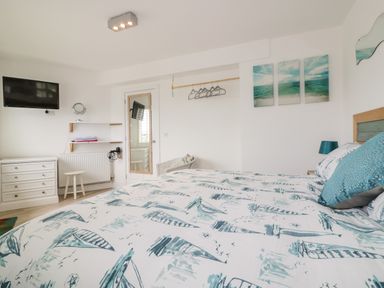 A bedroom with a bed covered in patterned bedding a wall-mounted television a chest of drawers and a full-length mirror at Fistral Drift in Newquay
