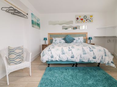 A bedroom with a double bed with patterned bedding two bedside tables with lamps a wicker chair with a cushion and wall art at Fistral Drift in Newquay