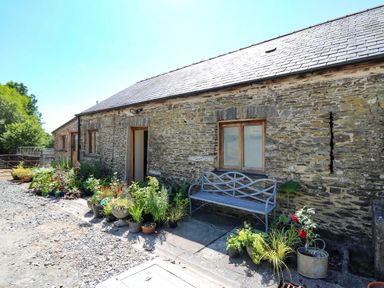 An exterior stone wall with windows and a door surrounded by various potted plants and a metal bench at Golwg Las in Pumsaint near Lampeter