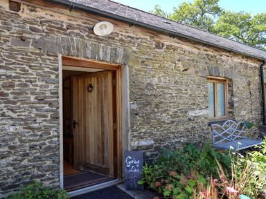 Stone exterior wall with an open wooden door a window a metal bench and plants at Golwg Las Pumsaint near Lampeter