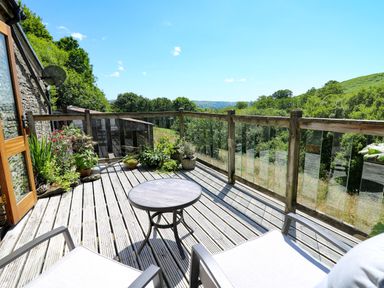 An outdoor deck with two chairs a round table potted plants and a wooden railing overlooking trees and hills at Golwg Las in Pumsaint near Lampeter