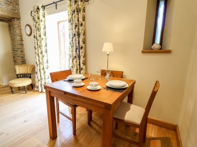 A dining area with a wooden table and four chairs set with white dishes and glasses at Golwg Las Pumsaint near Lampeter
