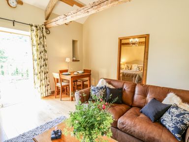 A living room with a brown leather sofa blue and floral cushions a wooden dining table set for four and a large mirror showing a bedroom at Golwg Las in Pumsaint near Lampeter