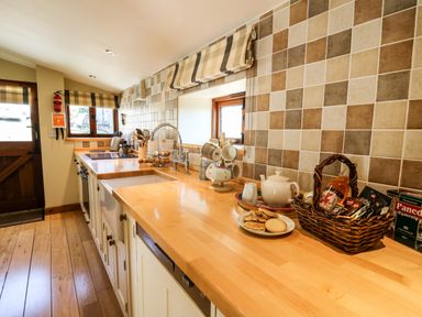 A kitchen with wooden countertops and tiled backsplash with a tea set and basket of snacks at Golwg Las in Pumsaint near Lampeter