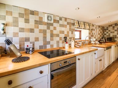 A kitchen with wooden countertops, white cabinets, an electric stove, an oven, utensils in a holder, a sink, a microwave, and a tiled backsplash at Golwg Las in Pumsaint near Lampeter