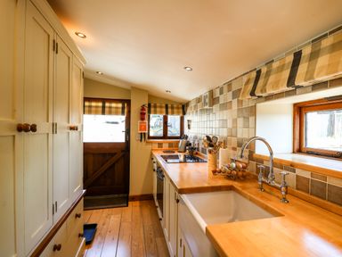 A kitchen with wooden countertops a white sink wooden cabinets and tiled walls at Golwg Las in Pumsaint near Lampeter