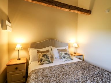 A bedroom with a bed between two bedside tables each with a lamp and a wooden ceiling beam at Golwg Las in Pumsaint near Lampeter