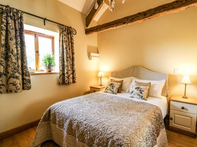 A bedroom with a double bed two bedside tables with lamps a window with curtains and exposed wooden beams at Golwg Las in Pumsaint near Lampeter