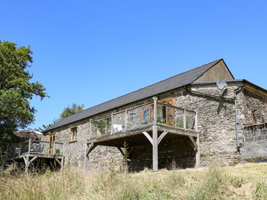 A stone building with two wooden balconies and glass railings with outdoor furniture and an umbrella at Golwg Las in Pumsaint near Lampeter