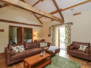 A living room with brown leather sofas a wooden coffee table and an open door leading outside at Nant Glas in Pumpsaint near Lampeter