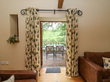 A doorway with floral curtains opening to a wooden deck with a table and chairs at Nant Glas Pumpsaint near Lampeter