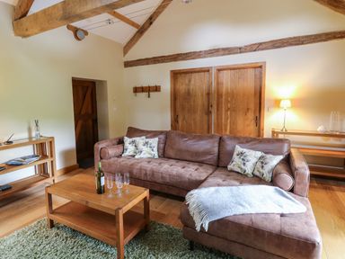 A living room with a brown sectional sofa and wooden coffee table with wine bottle and glasses at Nant Glas Pumpsaint near Lampeter