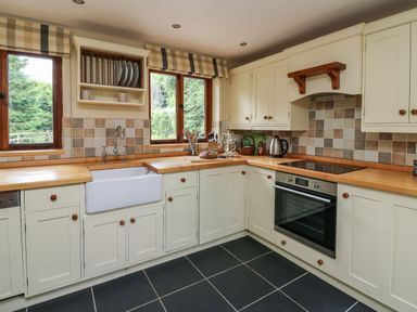 A kitchen with white cabinets wooden countertops a built in oven and two windows at Nant Glas Pumpsaint near Lampeter