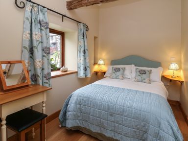 A bedroom with a bed and blue bedding two bedside tables and lamps and a small desk with a mirror at Nant Glas in Pumpsaint near Lampeter