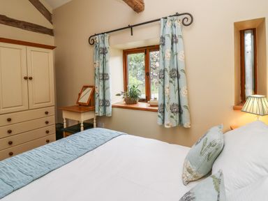 A bedroom with a bed pillows curtains a wardrobe dressing table and a window at Nant Glas in Pumpsaint near Lampeter
