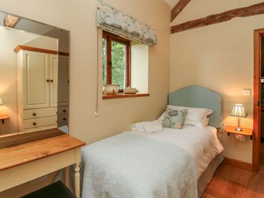 A bedroom with a single bed a bedside table with a lamp a dressing table and a window at Nant Glas in Pumpsaint near Lampeter