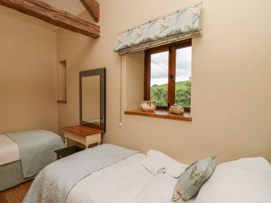 A bedroom with two single beds a window with a floral blind a small wooden table with a mirror and decorative pottery on the window sill at Nant Glas Pumpsaint near Lampeter