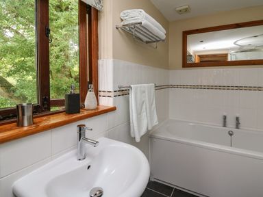 A bathroom with a white sink and bathtub a towel rack with towels and a window with soap dispensers at Nant Glas Pumpsaint near Lampeter