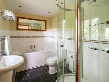 A bathroom with a bathtub, shower enclosure, toilet, sink, towel rack with towels, and a mirror at Nant Glas in Pumpsaint near Lampeter