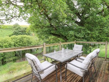An outdoor deck with a table and four cushioned chairs surrounded by trees at Nant Glas in Pumpsaint near Lampeter