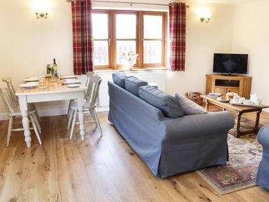 A living room with a dining table set with plates and glasses a blue sofa wooden floor and a television at The Cider House in Leominster