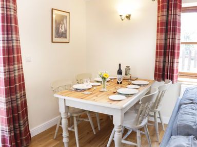 A dining area with a wooden table set for six and red plaid curtains at The Cider House in Leominster