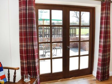 Wooden framed glass door with red plaid curtains and a wooden chair with a glass mug next to it at The Cider House in Leominster