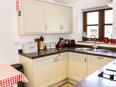 A kitchen corner with cream cabinets a bread box a knife block a red kettle a red toaster a plant by the window and a double sink at The Cider House in Leominster