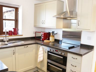 A kitchen with a sink a red microwave red pitchers a stove oven and white cabinets at The Cider House in Leominster