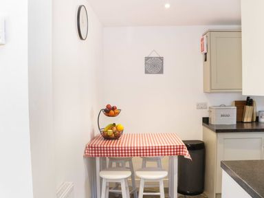 A kitchen corner with a small table covered with a red and white checkered tablecloth and white stools at The Cider House in Leominster