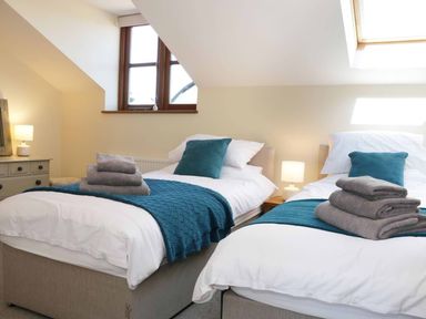A bedroom with two single beds with blue throws and gray towels at The Cider House in Leominster