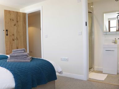 A bedroom with a bed covered with a blue blanket and folded towels a wooden door an open bathroom door with a sink and shower inside at The Cider House in Leominster