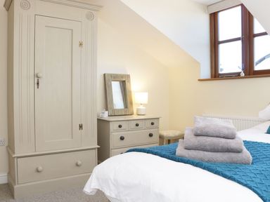 A bedroom with a wardrobe chest of drawers a lamp and folded towels on a bed at The Cider House in Leominster