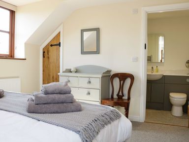 A bedroom with a bed folded towels on the bed a gray dresser a wooden chair and an open door showing a bathroom at The Cider House in Leominster