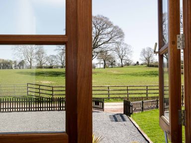 A view of a green field with trees and wooden fences through wooden open doors at The Cider House in Leominster