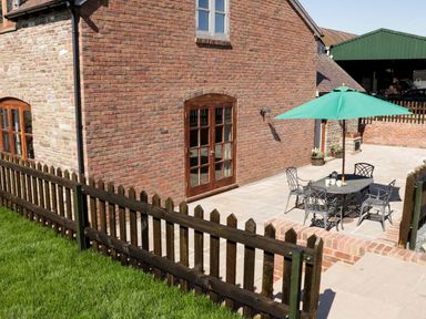 An outdoor patio area with a table four chairs and a green umbrella beside a brick building with wooden doors and windows at The Cider House in Leominster