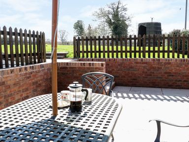 A patio with a metal table and chairs a coffee press and mugs on the table surrounded by brick walls and a wooden fence at The Cider House in Leominster
