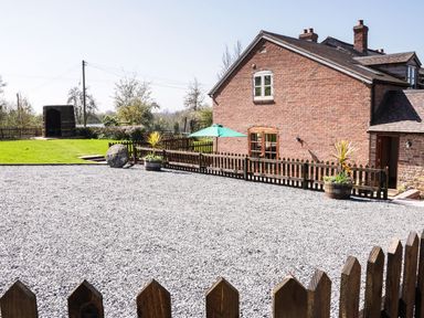 A brick house with a gravel driveway and wooden fence with potted plants and a lawn area at The Cider House in Leominster