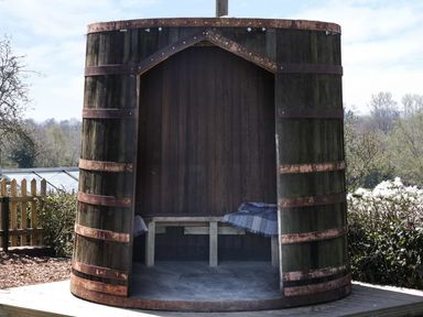 A large wooden barrel structure with an open front containing a wooden bench and blankets at The Cider House in Leominster
