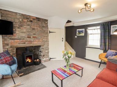A living room with a stone fireplace and wood stove a colorful coffee table and chairs at Kooky Cottage in Brecon
