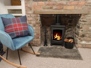 A rocking chair with a plaid pillow next to a wood burning stove in a brick fireplace at Kooky Cottage in Brecon