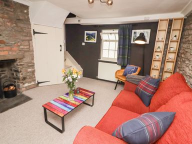 A living room with a red sofa, colorful coffee table, armchair, fireplace, and wooden shelves at Kooky Cottage in Brecon