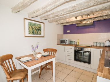 A kitchen with wooden chairs and table set for two a microwave oven and cooking utensils on the counter at Kooky Cottage in Brecon