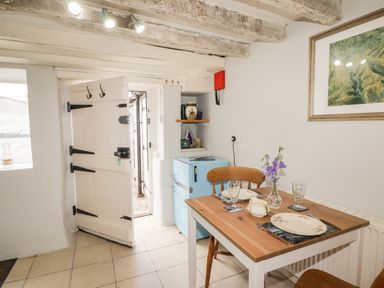 A small dining area with a wooden table set for two next to a light blue fridge and an open door at Kooky Cottage in Brecon