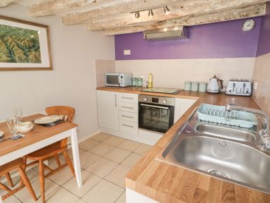 A kitchen with wooden countertops a sink a microwave a toaster kettle and a dining table with chairs at Kooky Cottage in Brecon