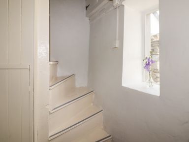 A small corner with beige stairs and a window with purple flowers at Kooky Cottage in Brecon