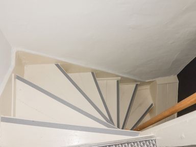 A narrow spiral staircase with metal strips on steps and a wooden handrail at Kooky Cottage in Brecon
