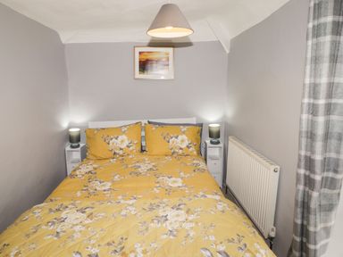 A bedroom with a bed with yellow floral bedding two bedside tables with lamps a radiator and a picture on the wall at Kooky Cottage in Brecon