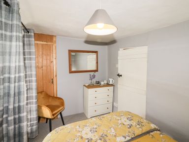 A bedroom with a bed with floral bedding a chair a chest of drawers with a kettle and cups and a mirror on the wall at Kooky Cottage in Brecon